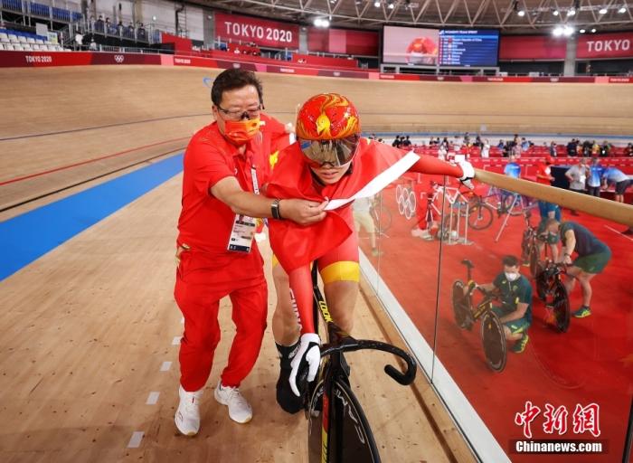 当地时间8月2日，场地自行车女子团体争先赛，钟天使和鲍珊菊组成的中国队击败对手，夺得金牌。图为教练为鲍珊菊披上国旗。图片来源：视觉中国